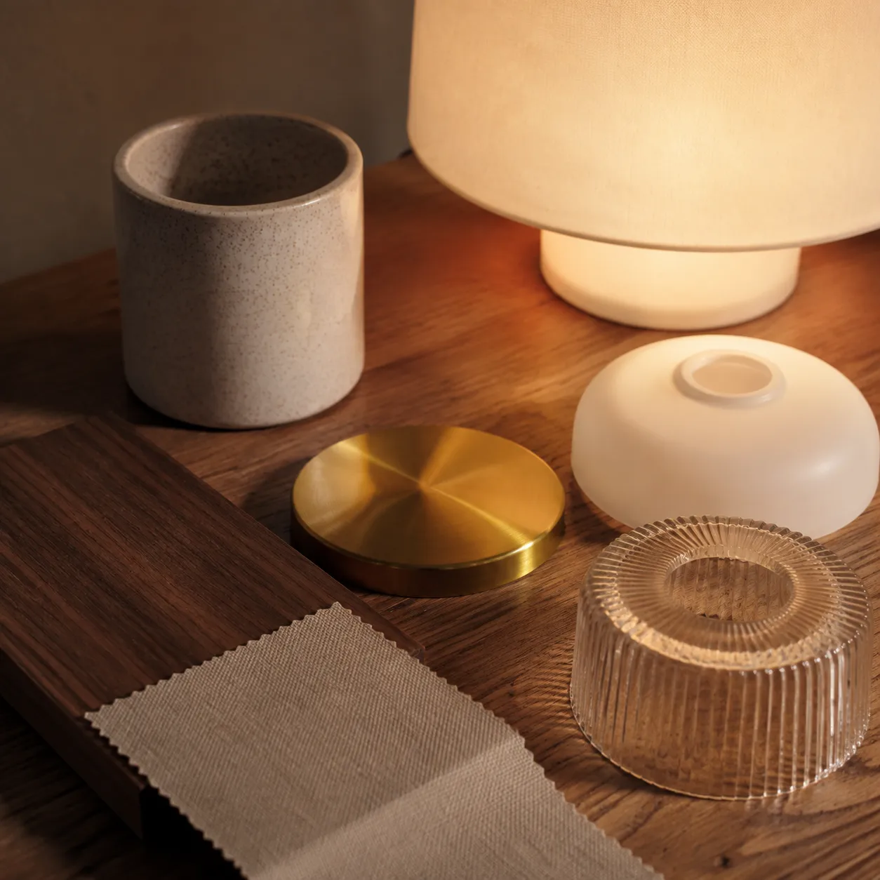 Ceramic, brass, walnut and opal glass lighting materials arranged beside a warm lamp glow